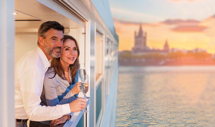 Middle aged couple sipping champagne in their balcony accommodations onboard an Emerald Waterways ship