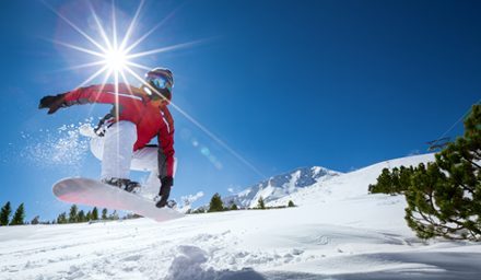 A guy snowboarding doing a trick in the air with a sunray in the background