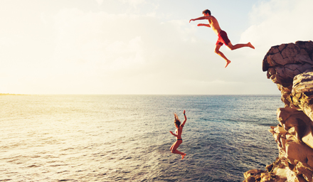 A young couple cliff jumping into the ocean