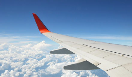 The wing of an airplane against a bright blue cloudy sky