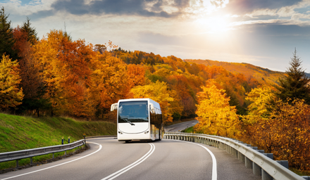 Motorcoach bus traveling on a windy road with Fall foliage in the background