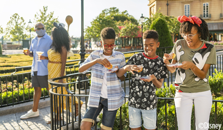 A family of three kids eating sweet treats with their parents walking and holding drinks in the background