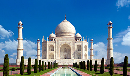 The Taj Mahal against a blue sky and lush green landscaping in the foreground
