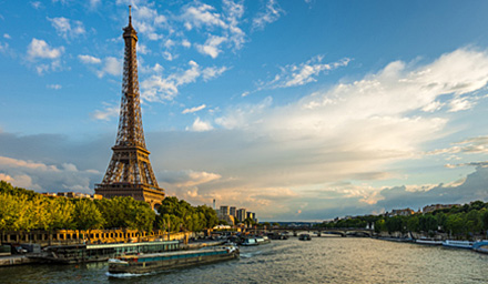 The Eiffel Tower on the left with a river and river boats on the right on a bright day
