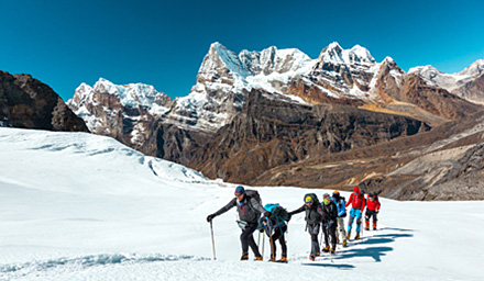 A group of cross country skiers traveling up a snow covered mountain with rocky mountains in the background