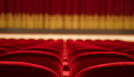 Red theatre seats with red curtain closed on stage