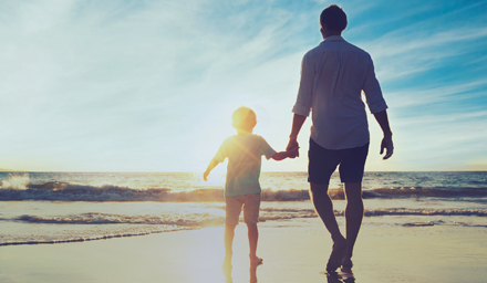 A man and child walking on the beach at sunset