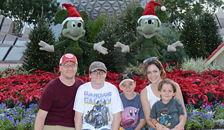 Cute family of 5 at Epcot at Walt Disney World in Florida during the holiday season sitting in front of Mickey and Minnie topiary