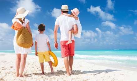 Family of four walking on the beach with their backs towards us walking towards the tropical beach