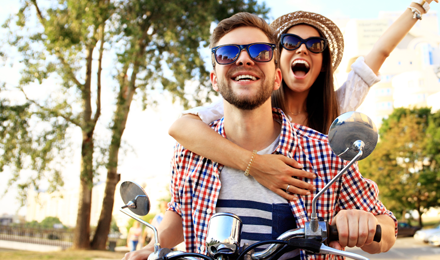 A couple riding on a scooter with the woman raising her hand and cheering