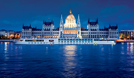 Uniworld river cruise on blue water with Hungry Parliament building in the background at night