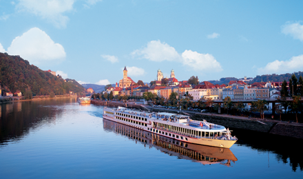 Viking river cruise on the water with a city right next to it while the sun is rising